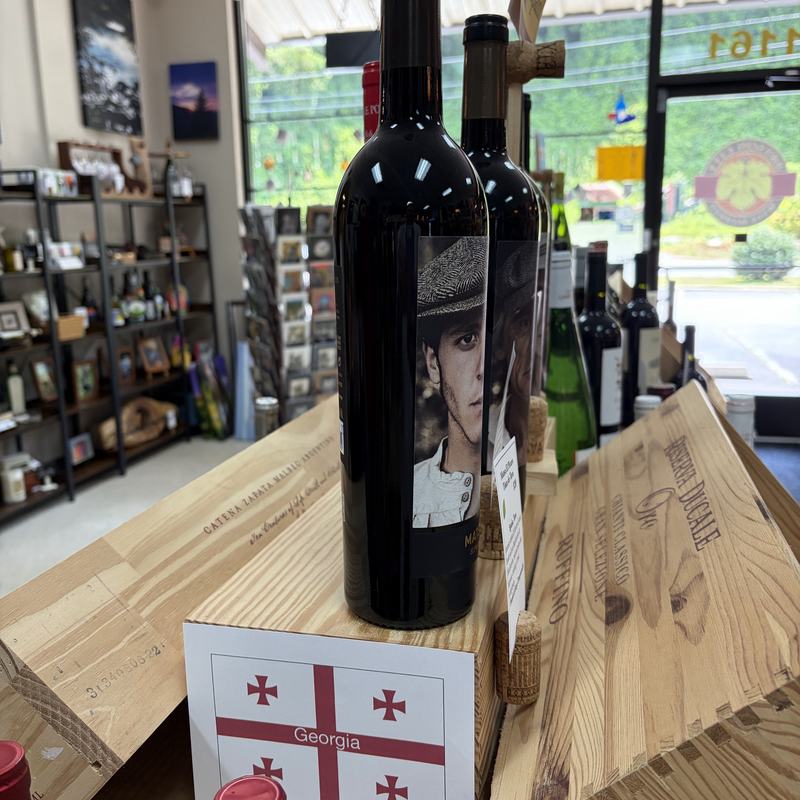A large format wine bottle on a wooden display crate near the front window, with daylight and Main Street beyond