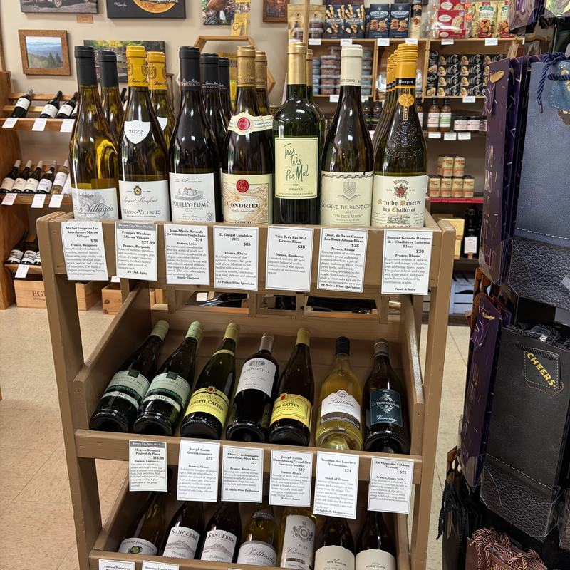 A wooden rack of white wine bottles, each with a handwritten shelf card describing the wine