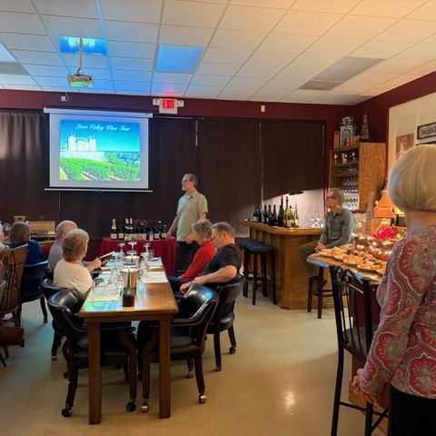 The back tasting room set with long tables and glassware, a class in progress and a food spread laid out along the bar